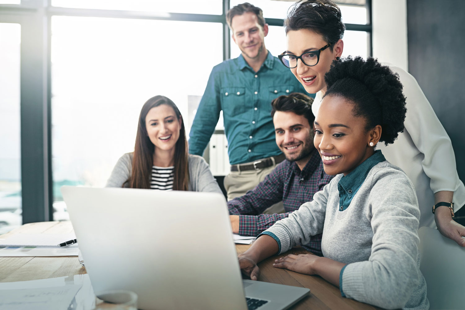 A group of colleagues smiling as they look at a laptop screen.