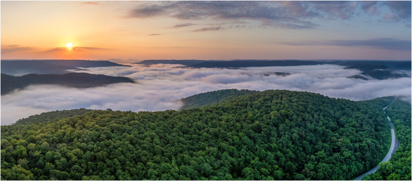 Aerial view of landscape covered in mist with setting/rising sun in the distance 