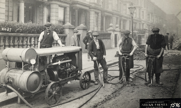 Historical image of workers handling machines on a road.